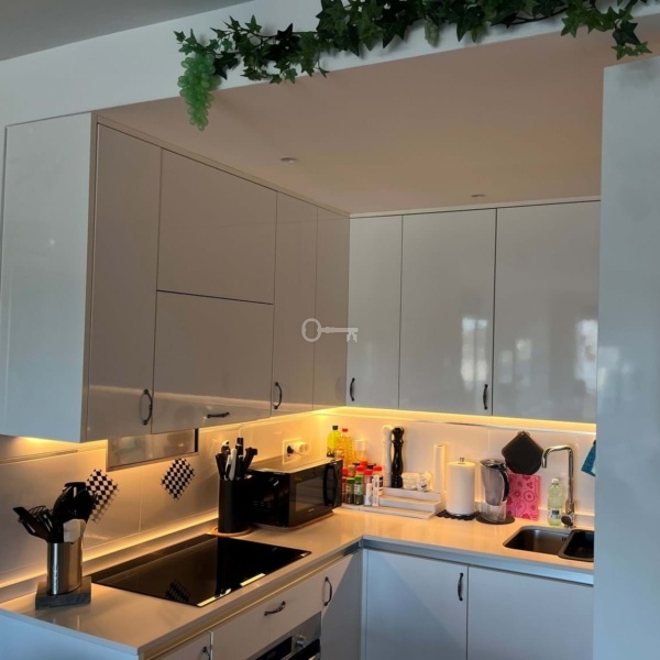 Nowoczesna kuchnia z oświetleniem LED, białe szafki i akcesoria kuchenne. Idealna przestrzeń do gotowania i codziennych posiłków.
