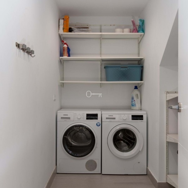 Pralka i suszarka w pralni z białymi półkami na detergenty i akcesoria.