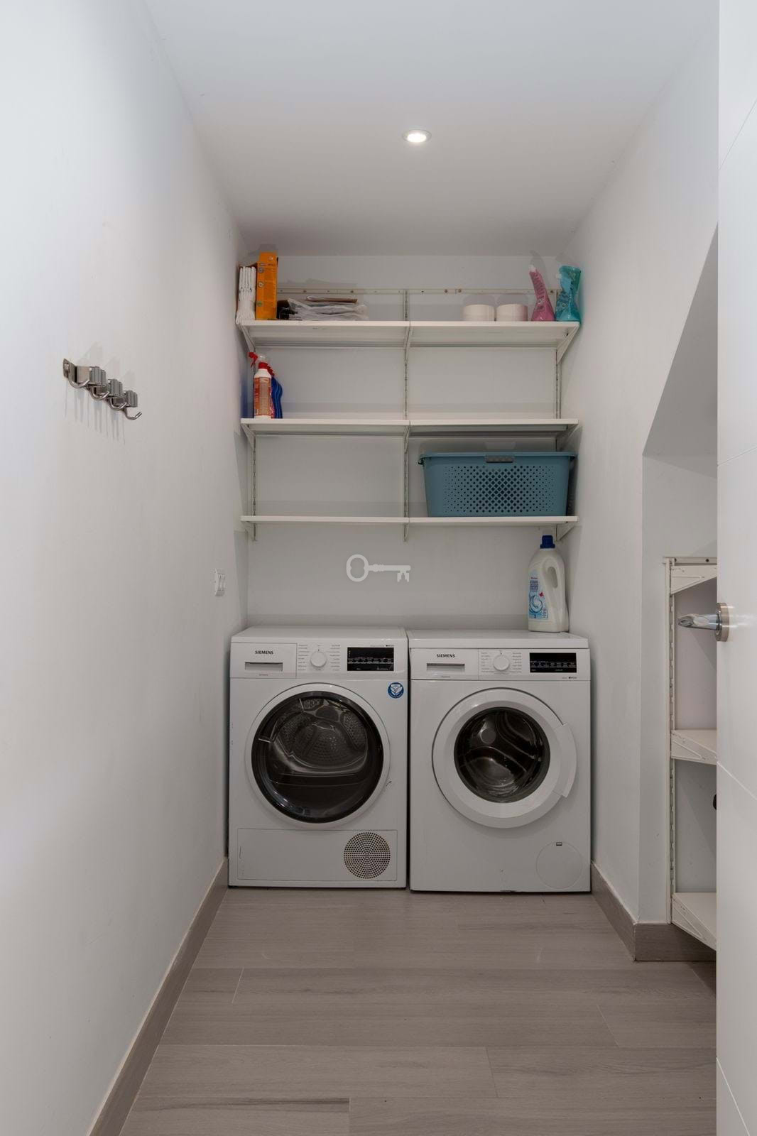 Pralka i suszarka w pralni z białymi półkami na detergenty i akcesoria.