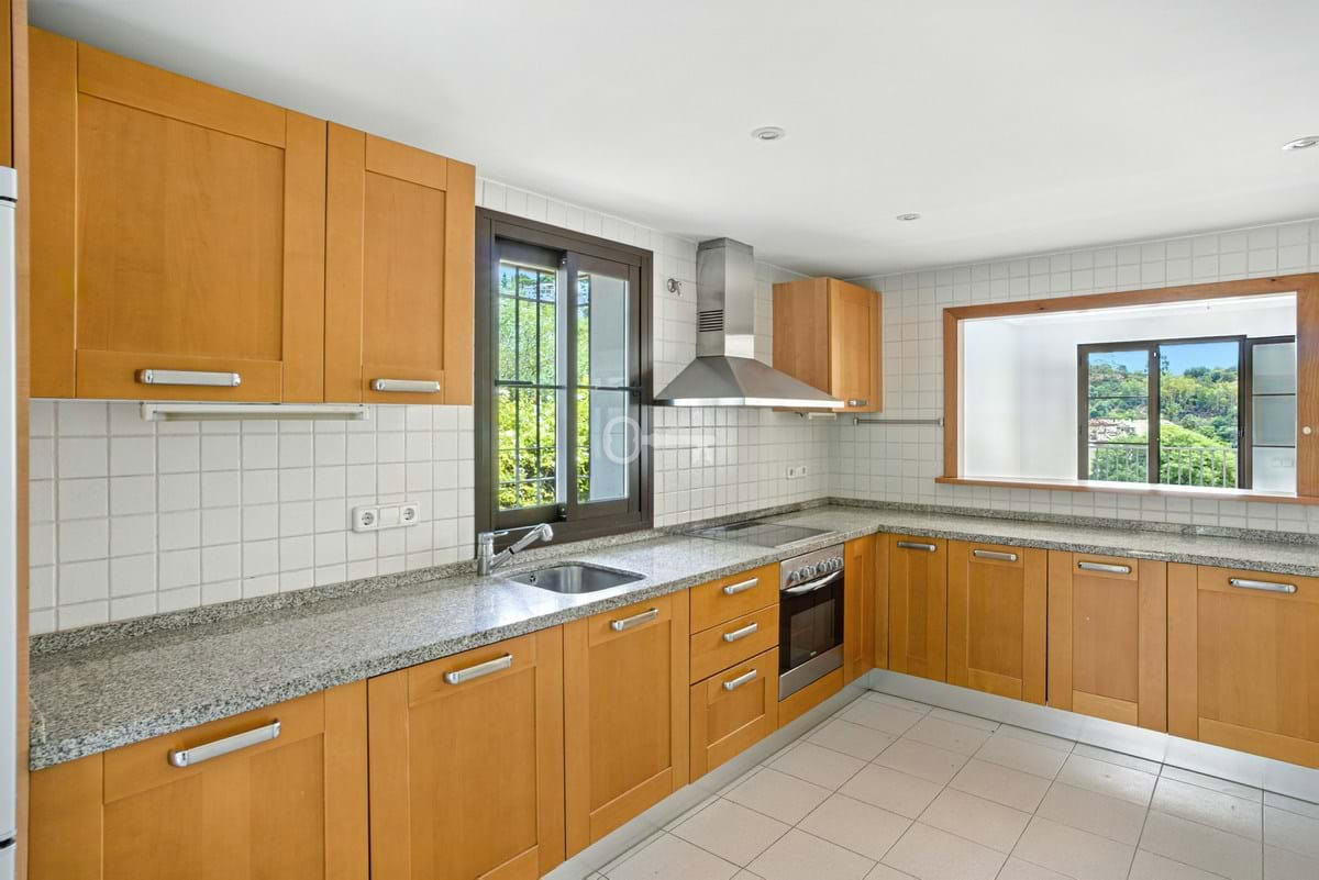 Nowoczesna kuchnia z drewnianymi szafkami i dużym oknem, idealna do gotowania i relaksu.