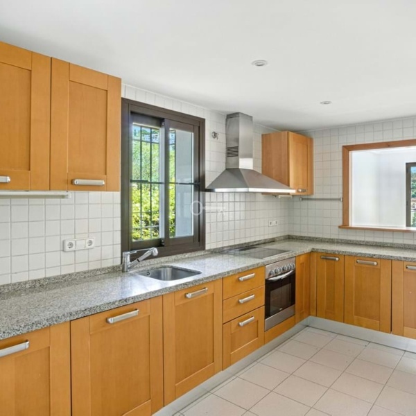 Nowoczesna kuchnia z drewnianymi szafkami i oknami z widokiem na zieleń.