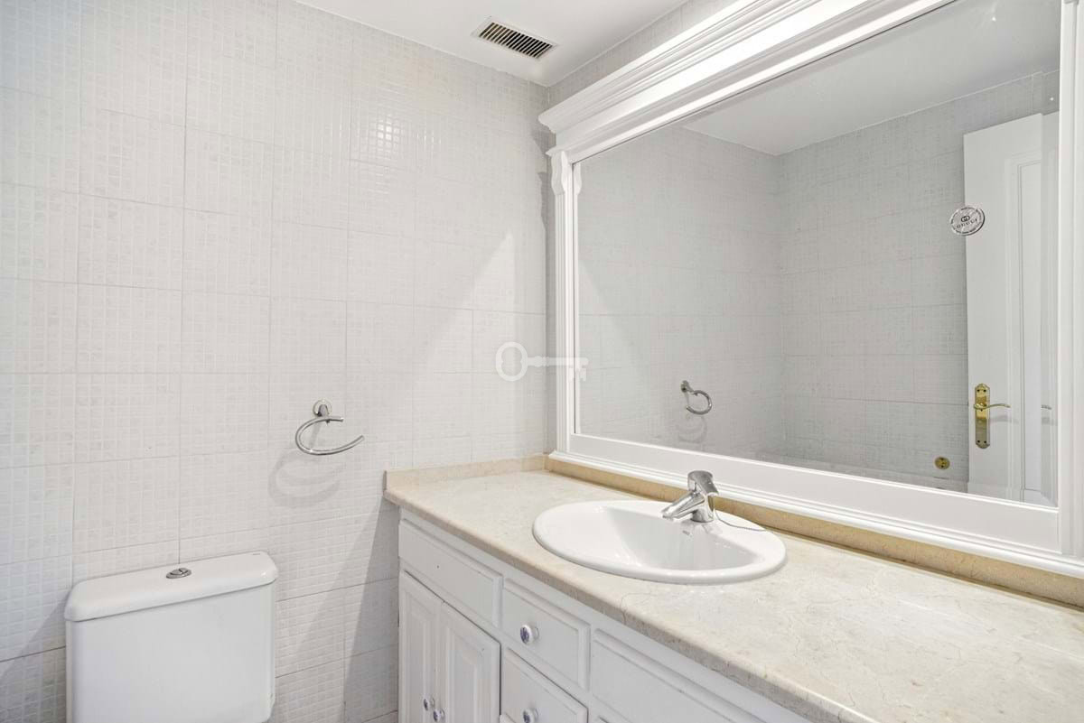 Nowoczesna łazienka z dużym lustrem, umywalką i białą armaturą w eleganckim stylu.