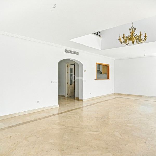 Przestronne wnętrze mieszkania z białymi ścianami i marmurową podłogą.