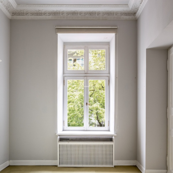 Stary biały okno w białej ścianie z ozdobną gipsową listwą na suficie.