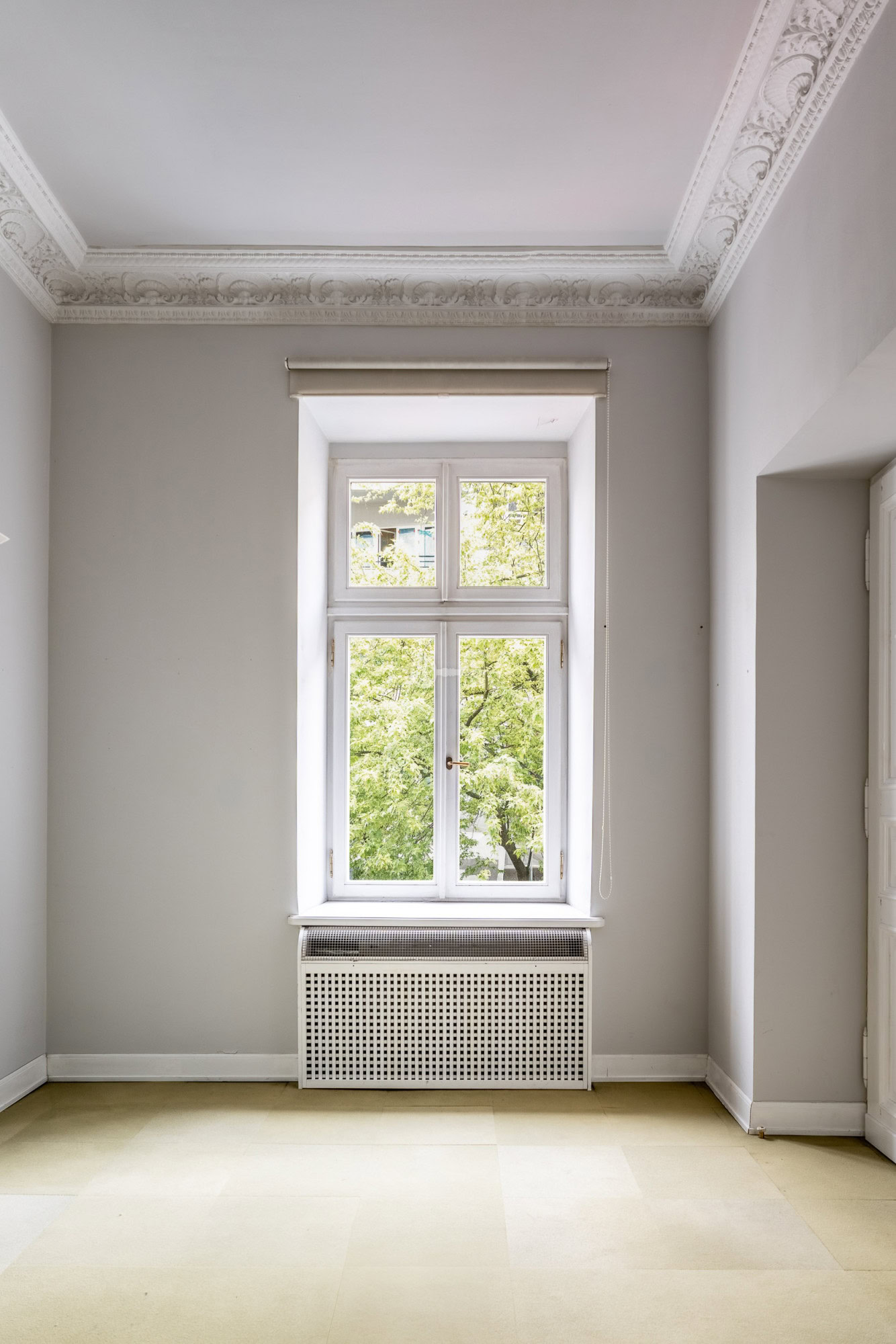 Stary biały okno w białej ścianie z ozdobną gipsową listwą na suficie.