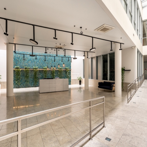 Przestronne lobby nowoczesnego biurowca z eleganckim wykończeniem i zielonymi akcentami.