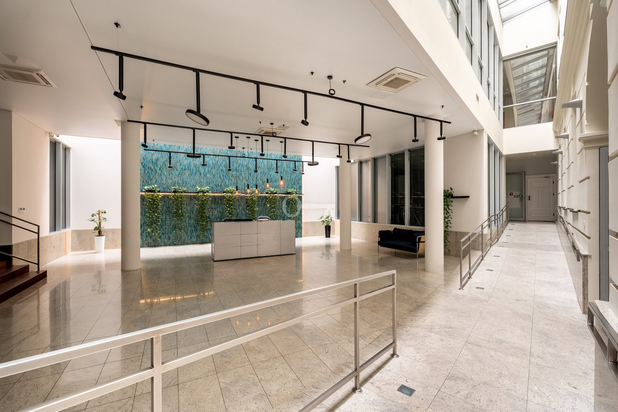 Przestronne lobby nowoczesnego biurowca z eleganckim wykończeniem i zielonymi akcentami.